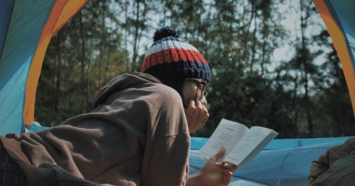 Girl reading a book while camping in a tent